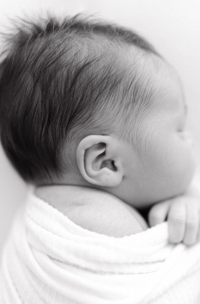 A black and white close up of a newborn baby's ear and hair. 
