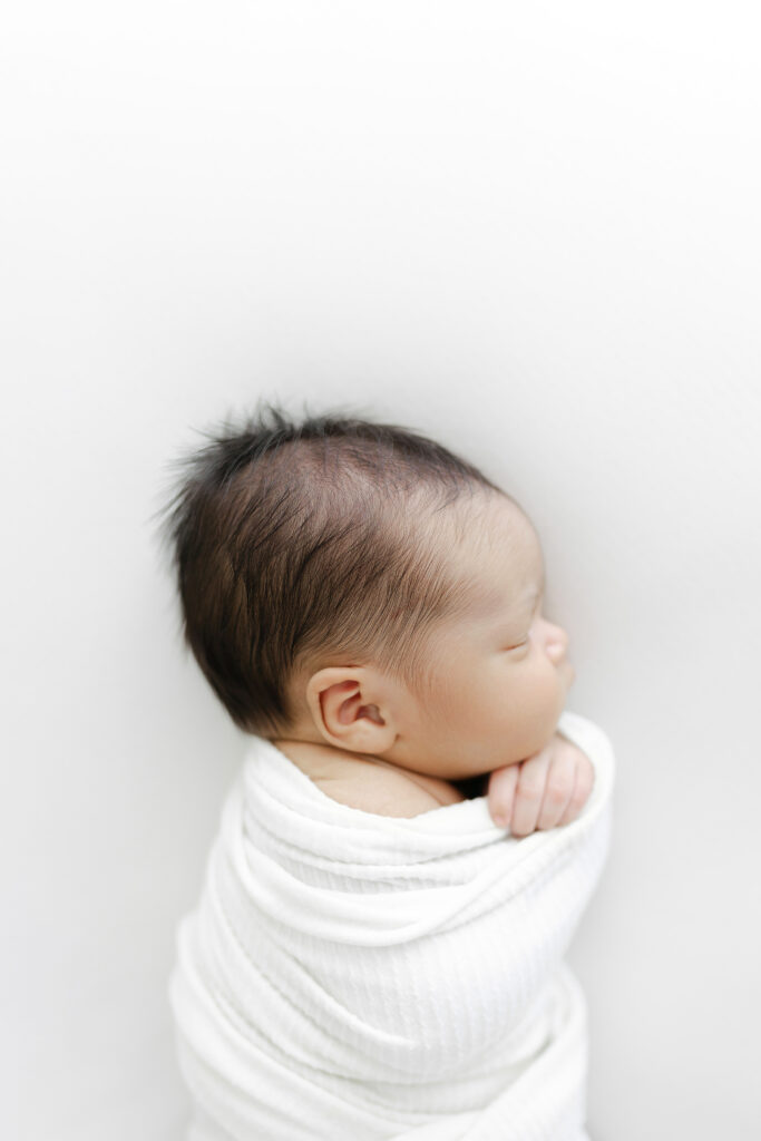 A newborn baby boy sleeping on a white background during his newborn photography session. 