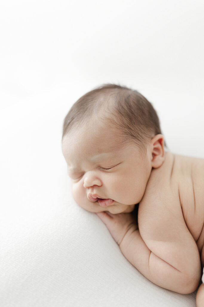 A newborn baby boy sleeping on his stomach on a white background during his newborn photography session. 
