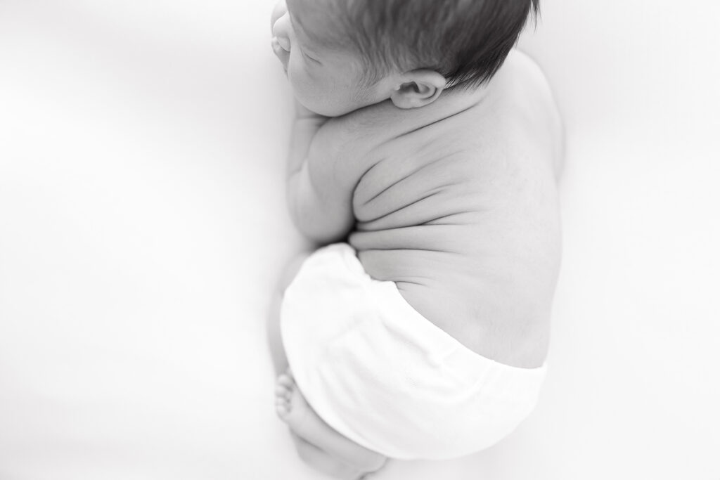 A black and white photo of a baby laying on his stomach and a white background. 
