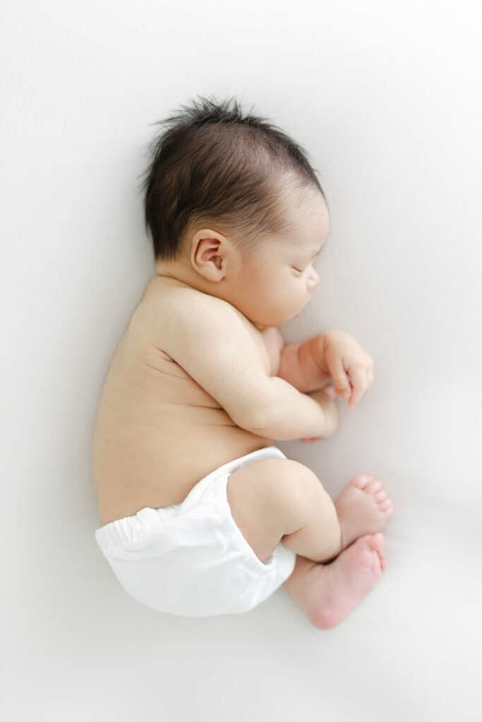 A newborn baby boy sleeping his side on a white background during his newborn photography session. 