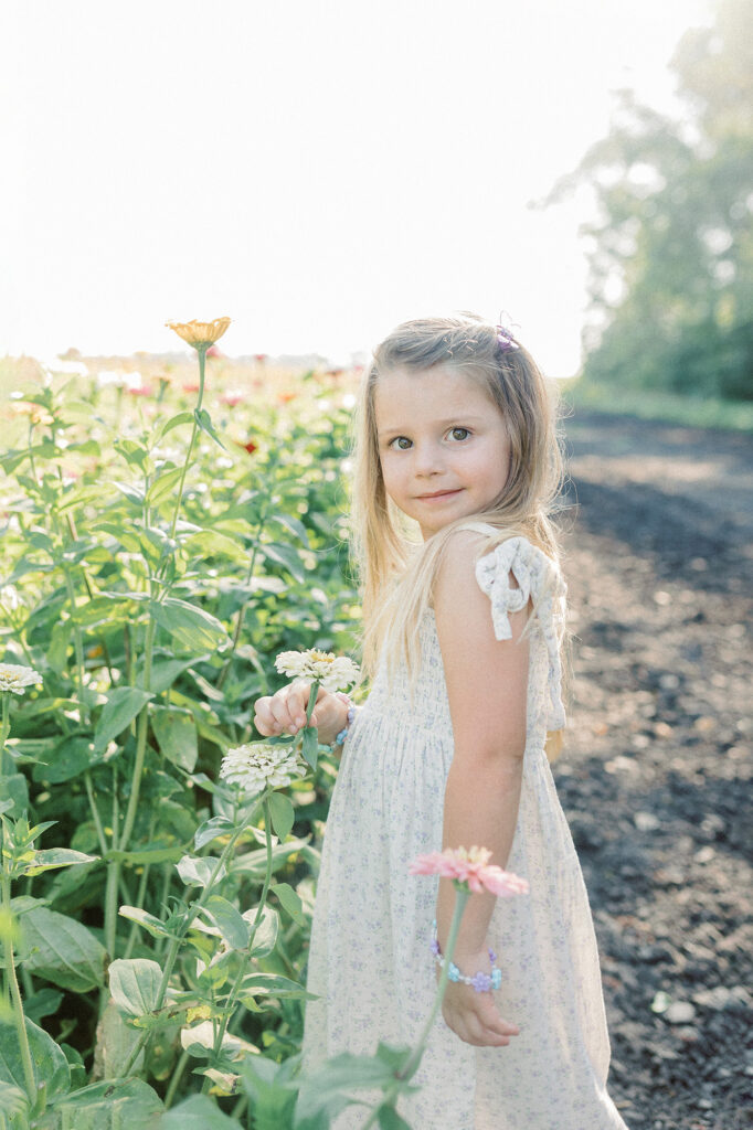 A young girl smiling at the camera while standing in a flower field during a sunset photography session. 