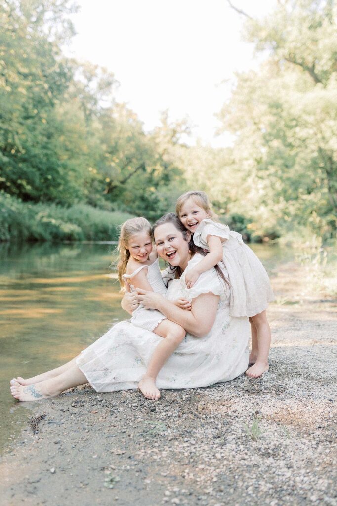 A mom and her two daughters sitting on a river bank for family photography in grand forks