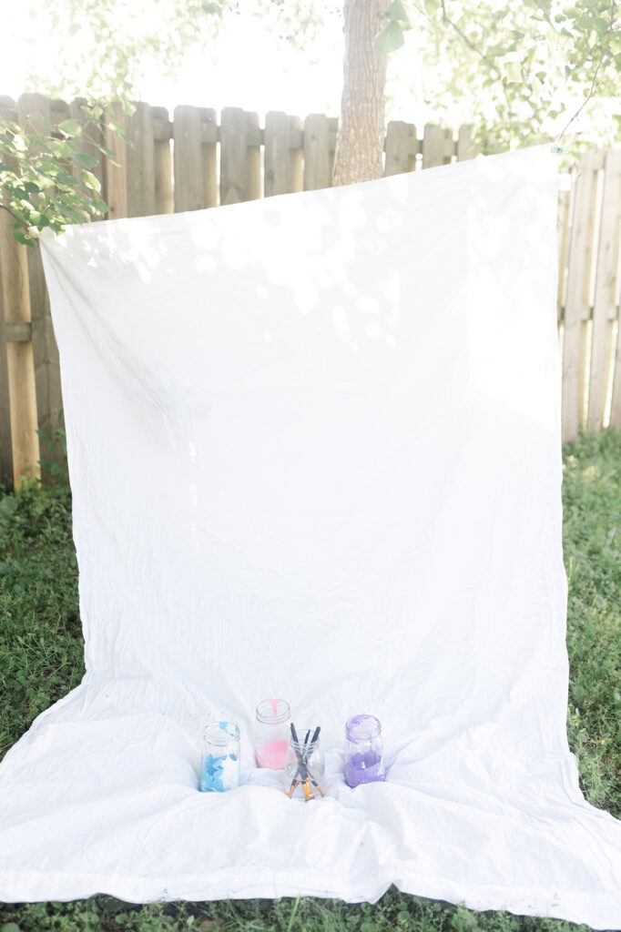 A blank white sheet with mason jars full of paint before kids get creative during their photo session.