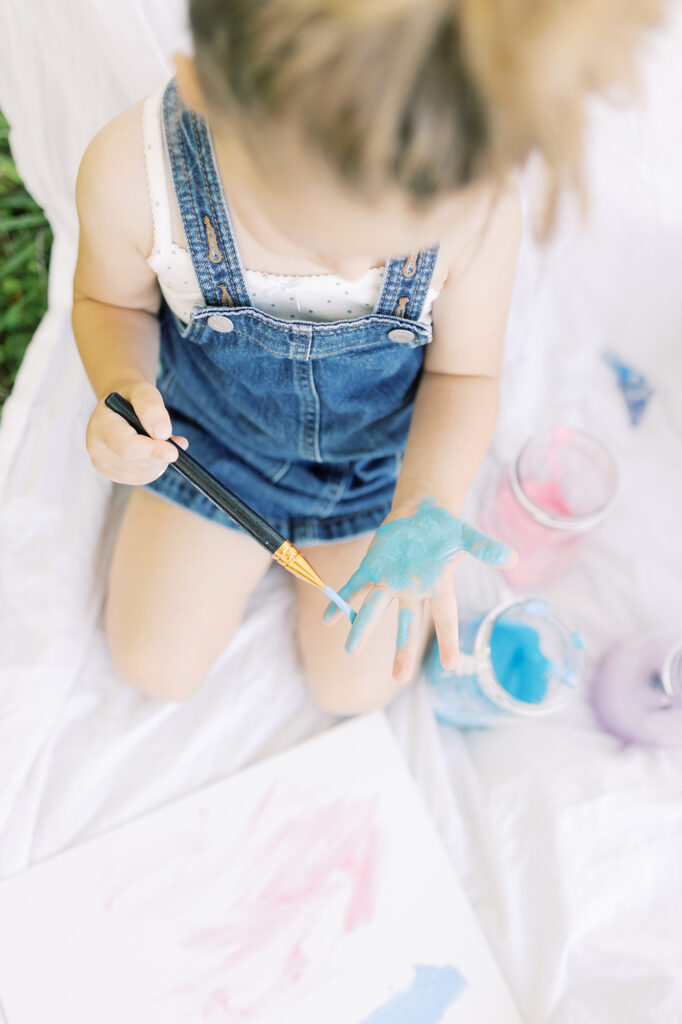 A young girl girl painting her hands with blue paint during her creative painting photo session.