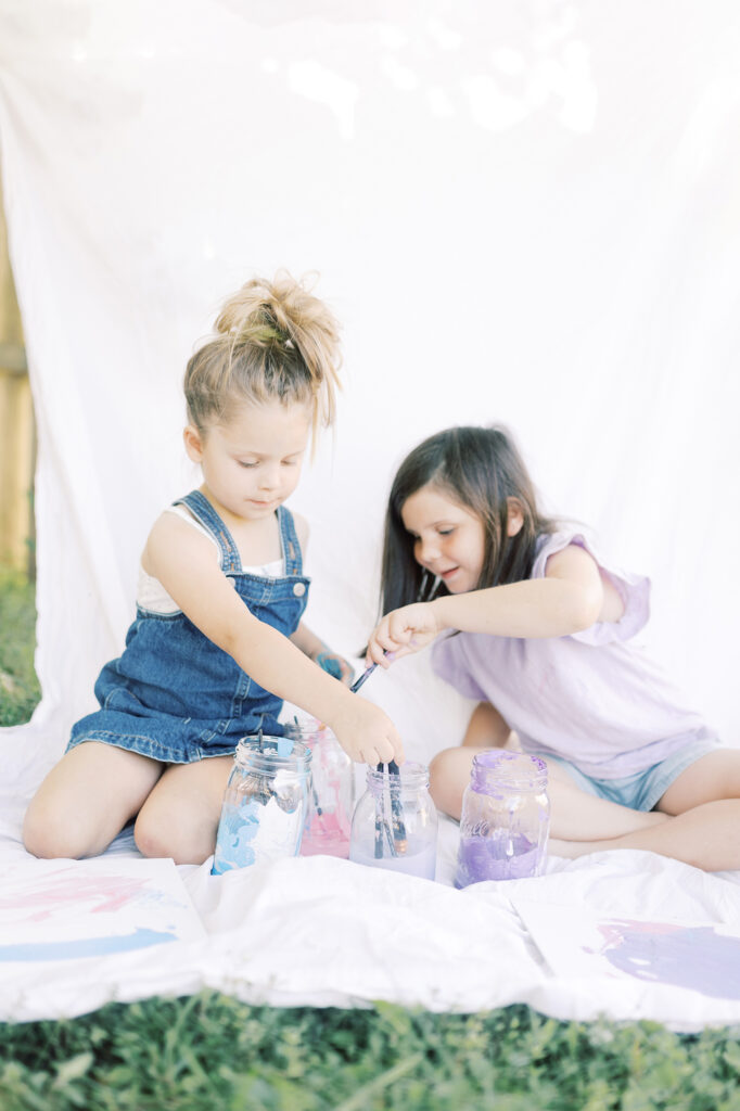 Two young girls sitting on a sheet being creative with paint during their photography session.