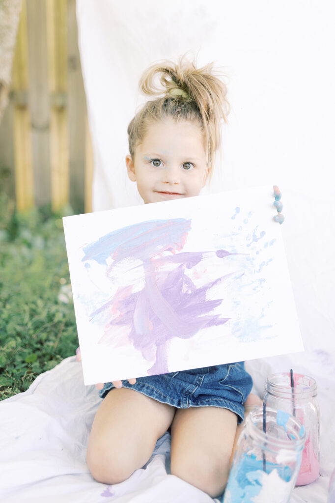 A young girl holding up a painting she created.
