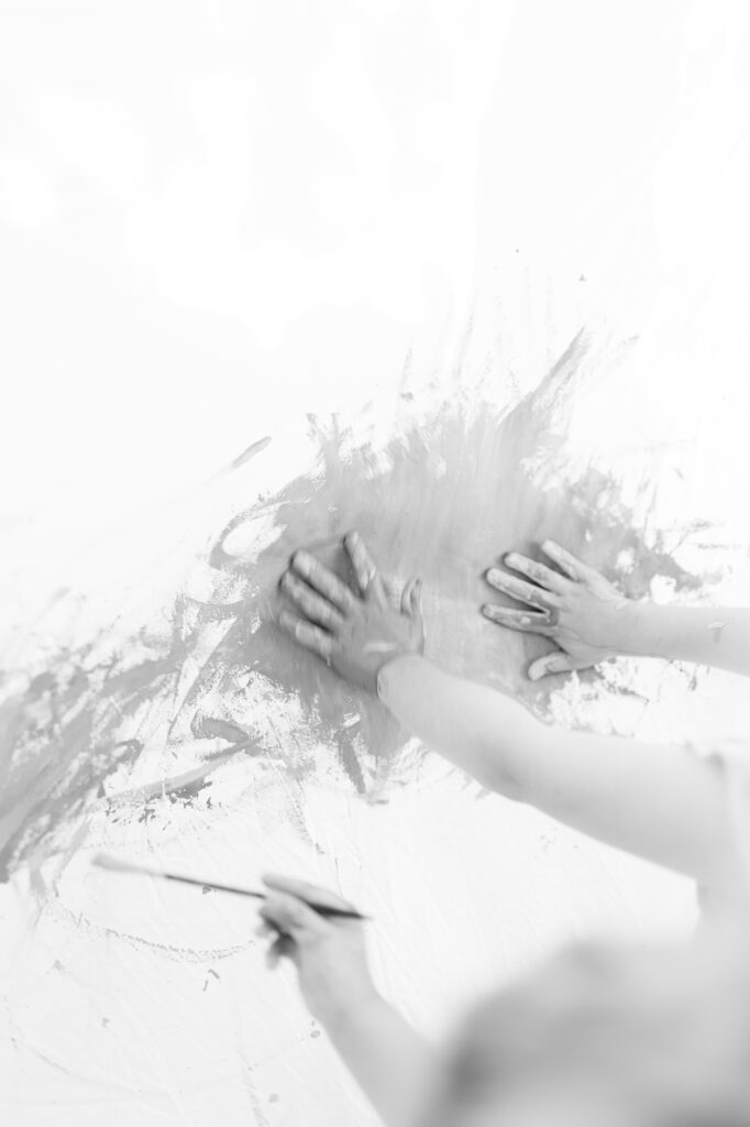 A black and white photo of a young kid's hands spreading paint on a canvas for a creative photo.
