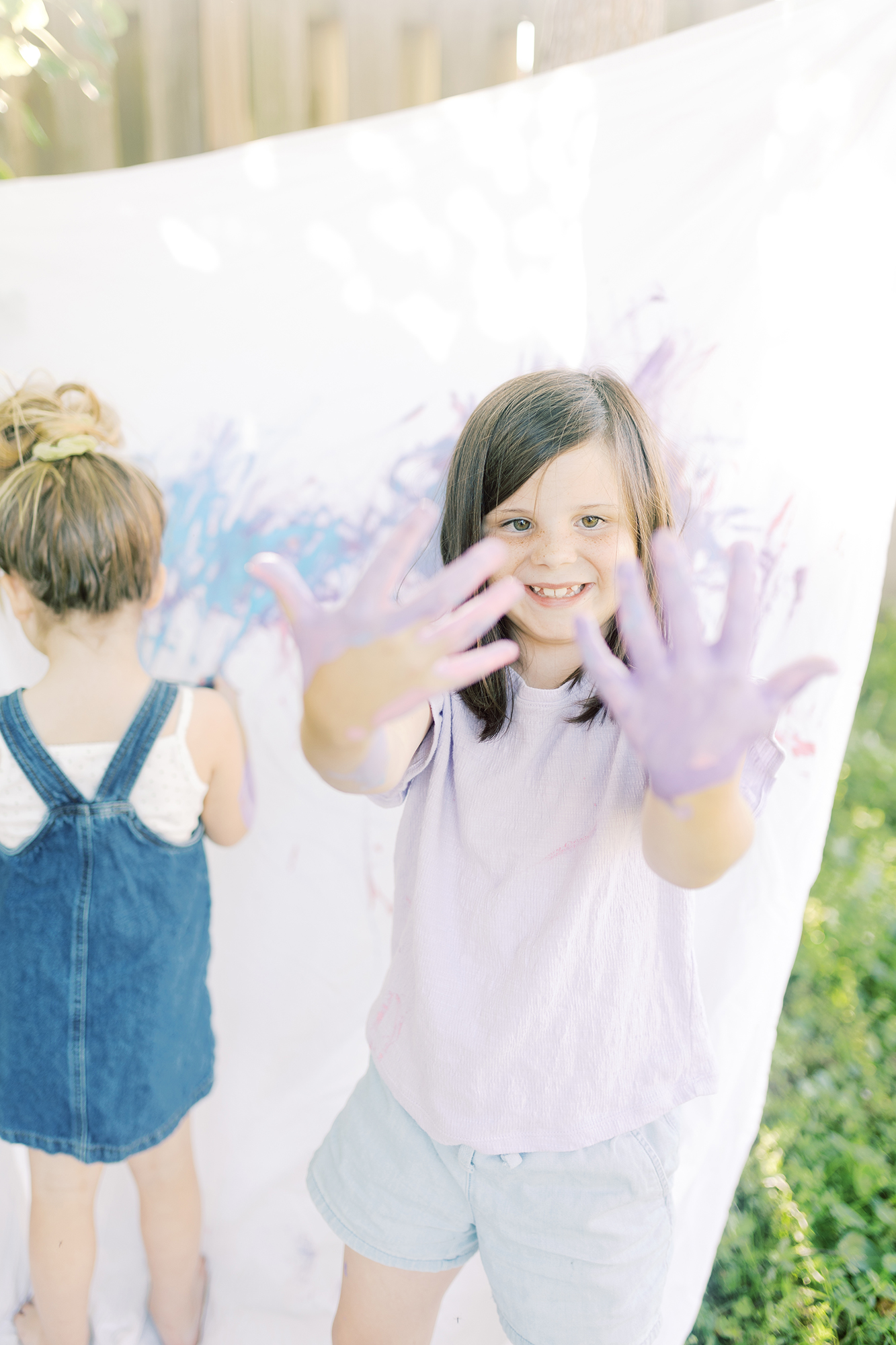 A young girl holding up her hands covered in purple paint after creative photo session.