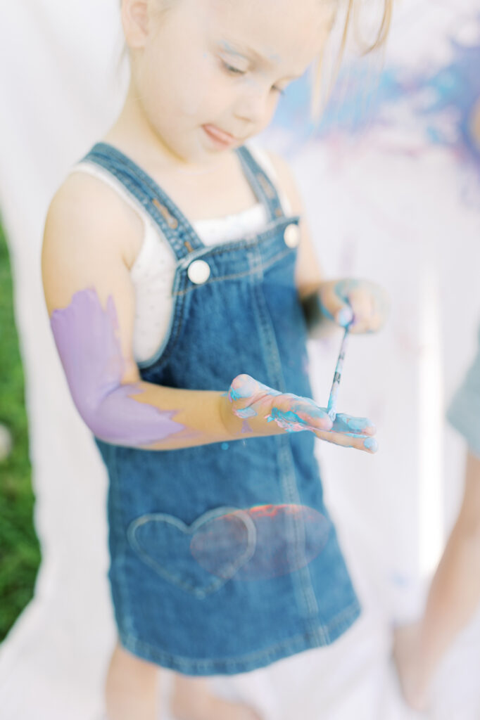 A little girl using a paint brush to paint her hand to make art.