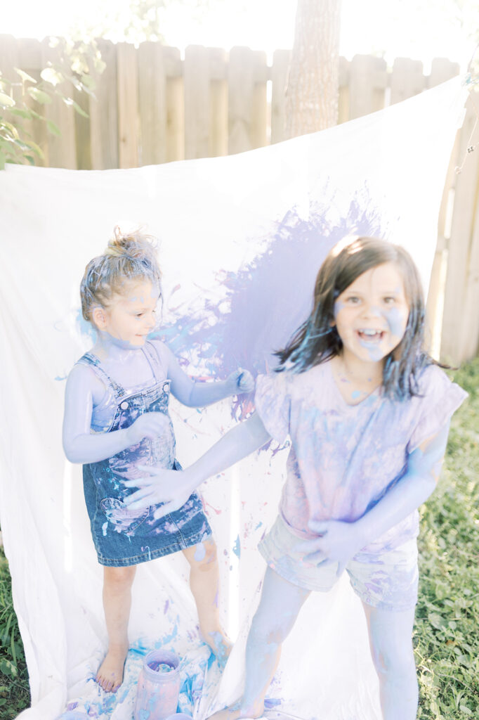 Two young girls laughing and throwing paint on each other during their painting photo session.
