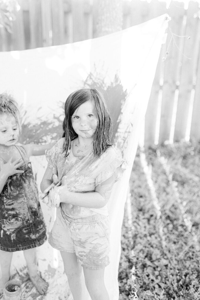 A black and white photo of a young girl covered in paint after her creative painting photo session.