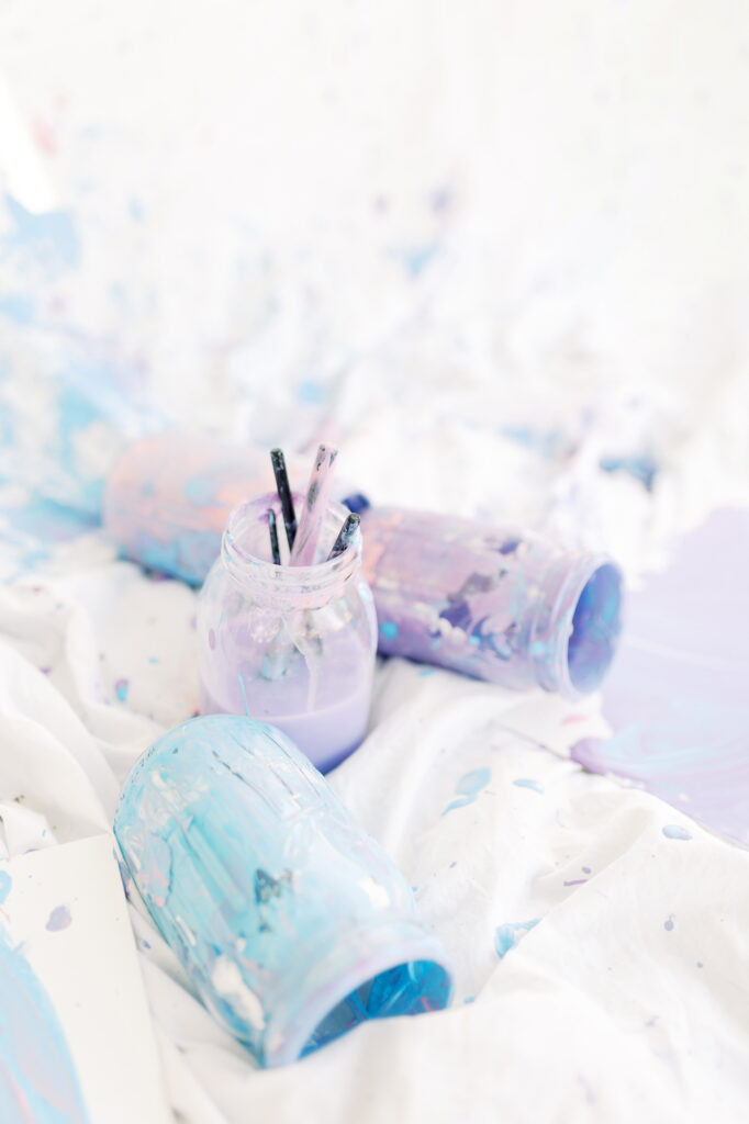 Mason jars with paint brushes and paint on a canvas after a unique photo session.