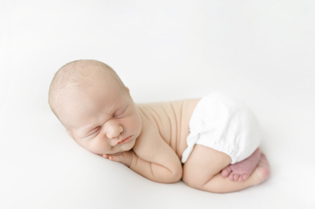 Newborn baby posed on their tummy highlighting soft rolls and delicate features