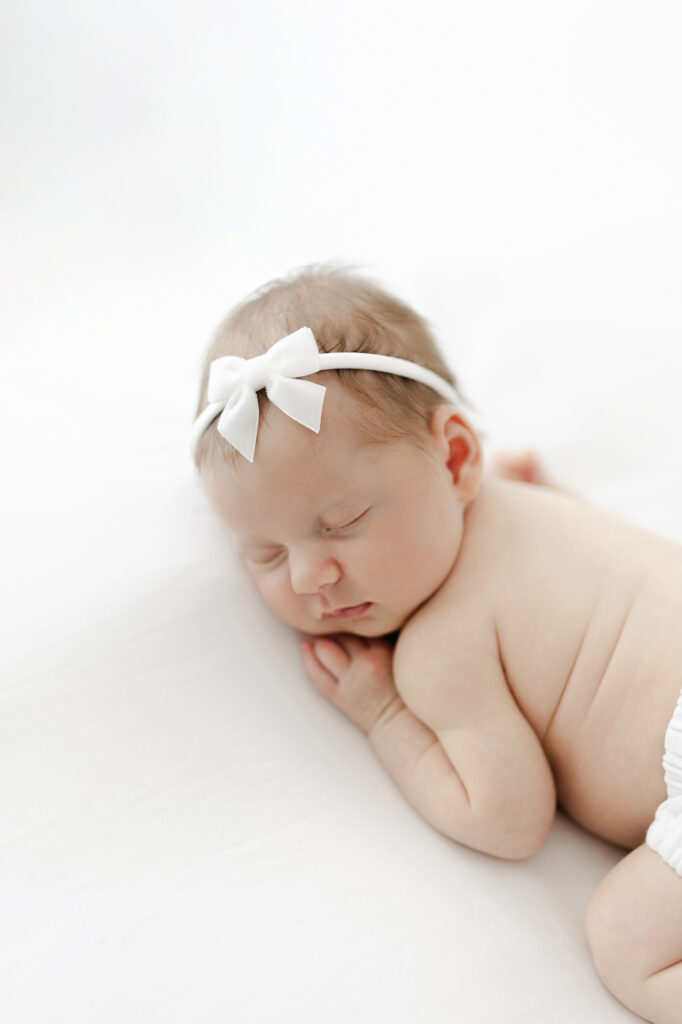 Baby on tummy during newborn photography session showing tiny rolls and profile.