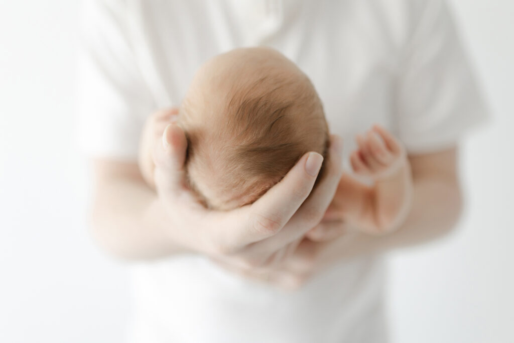 Close-up newborn photo capturing baby’s hair and size in dad’s hands